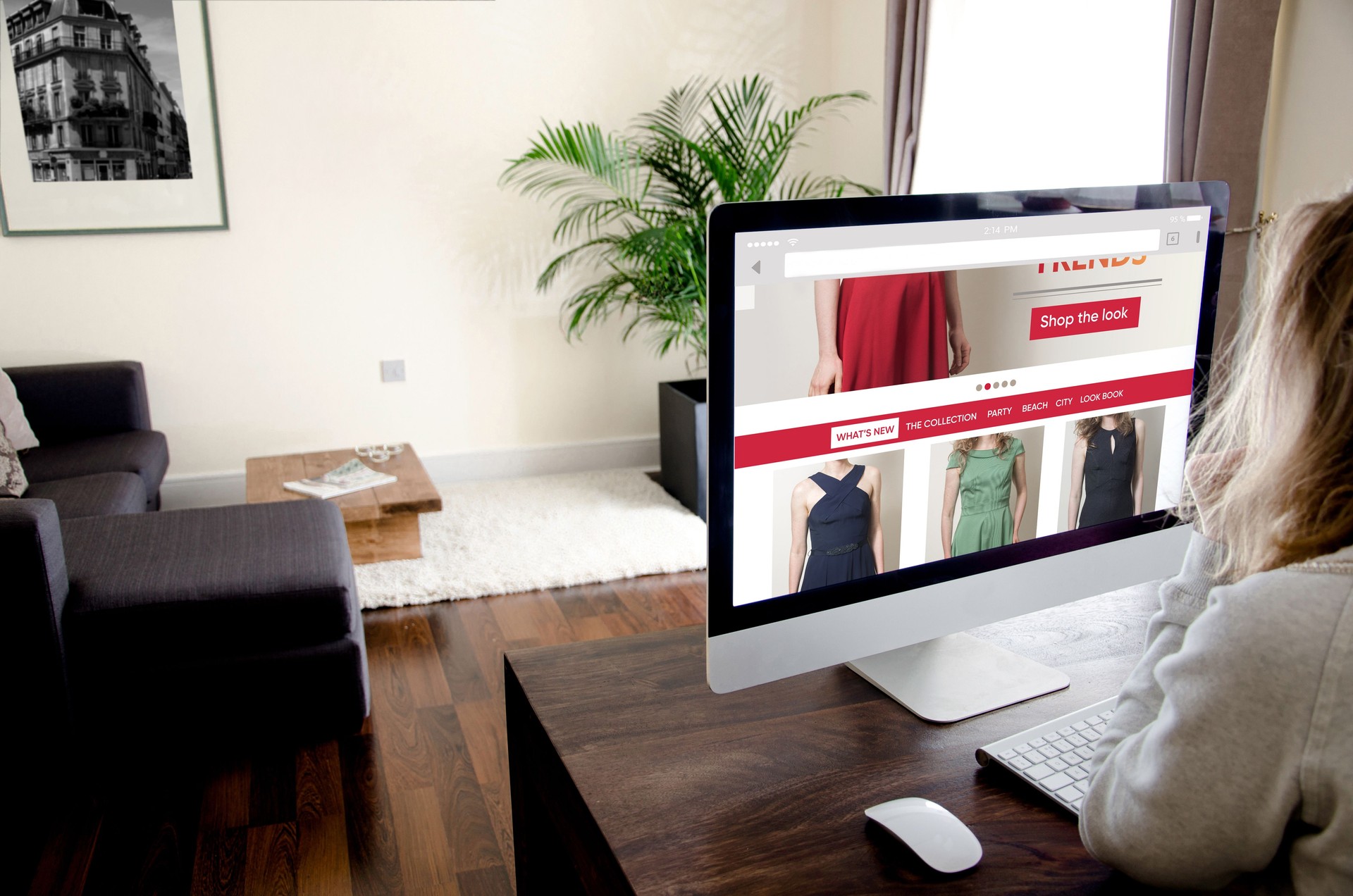 Young woman sitting at home on a desk in front of a desktop pc choosing clothes on the internet